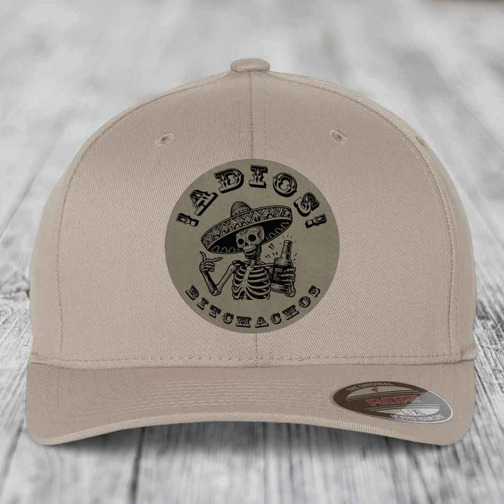 Beige baseball cap with circular patch featuring skeleton in sombrero holding beer, text &