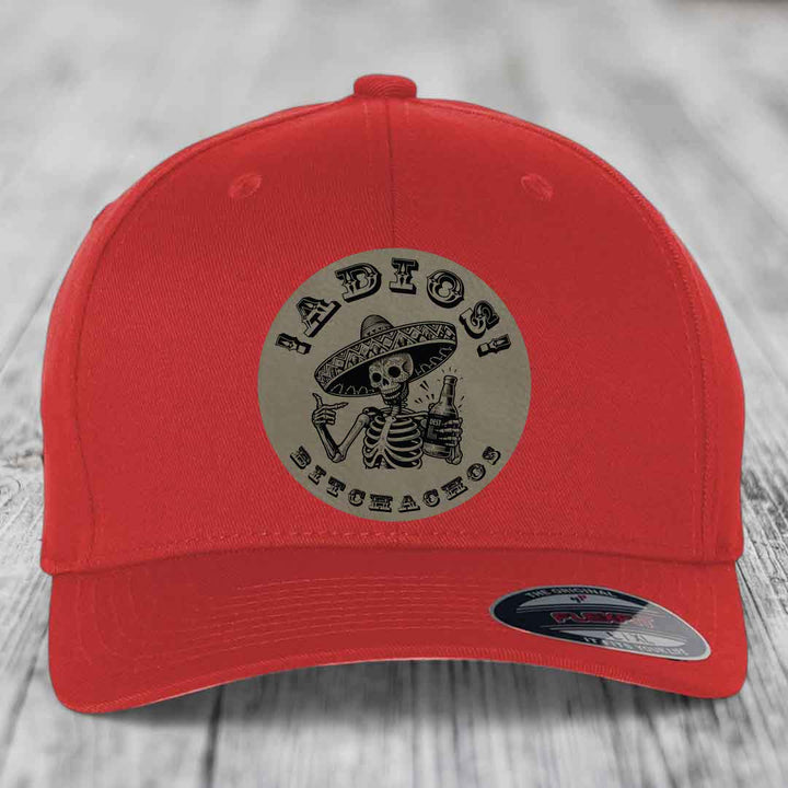 Red baseball cap with circular patch featuring skeleton in sombrero holding beer bottle and text &