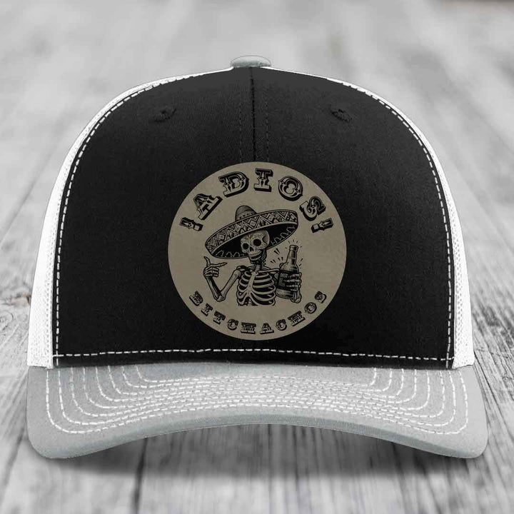 Black and white trucker hat with a circular leather patch featuring a skeleton in a sombrero holding a beer bottle.