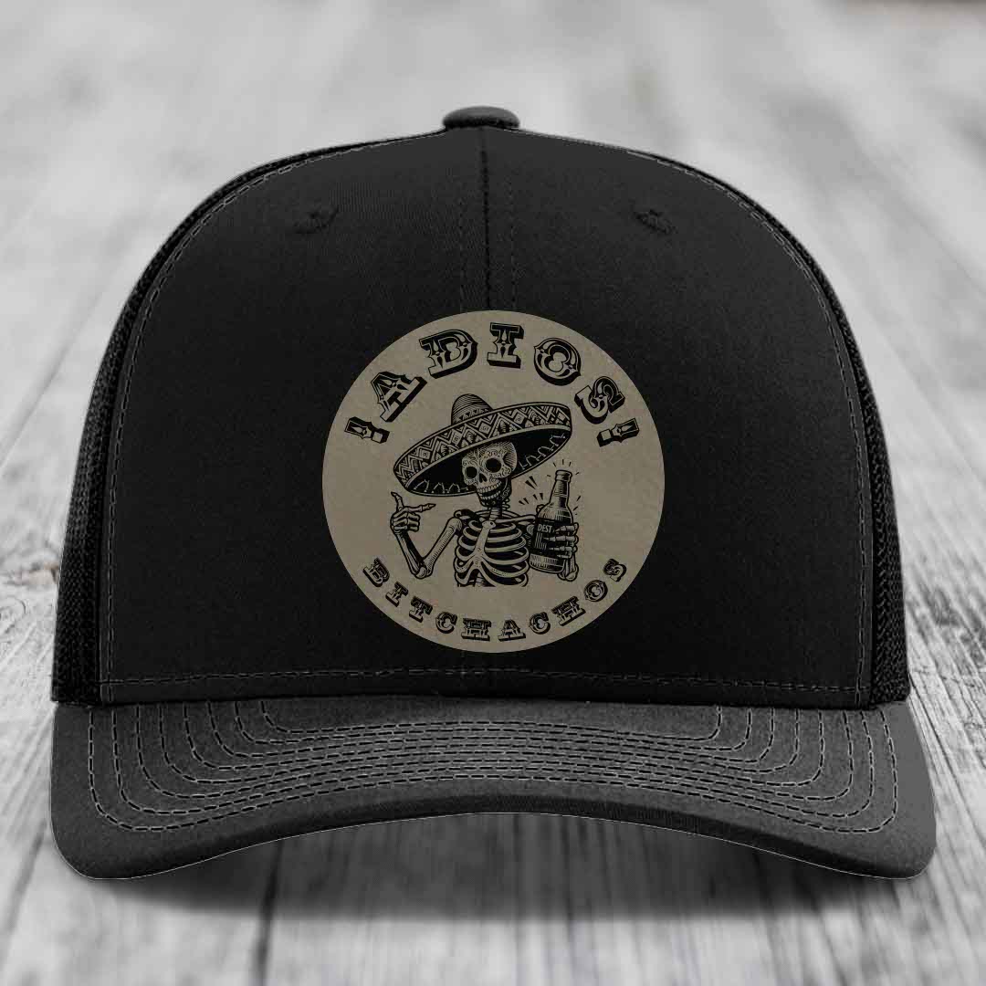 Black trucker hat with circular beige patch featuring skeleton in sombrero holding beer bottle and text &