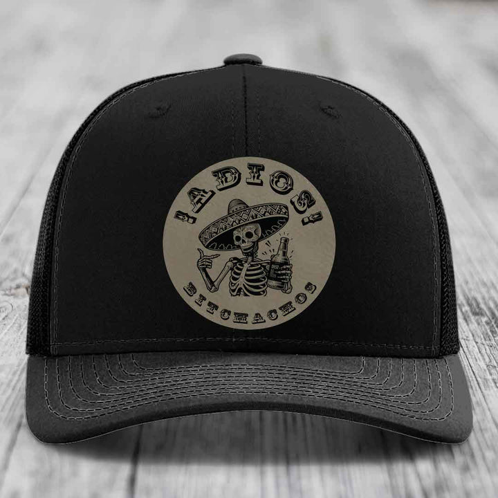 Black trucker hat with circular beige patch featuring skeleton in sombrero holding beer bottle and text &