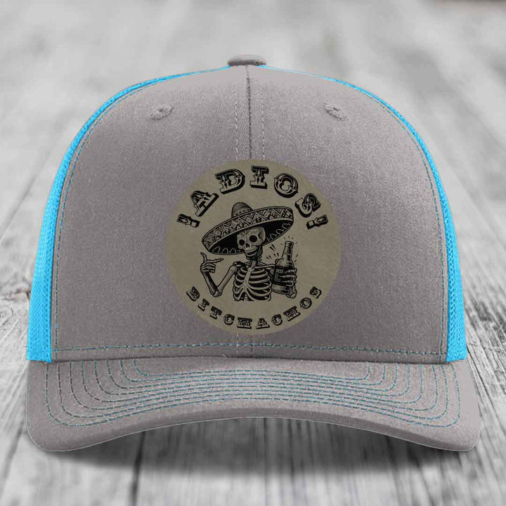 Grey trucker hat with blue mesh back and embroidered skull patch reading &