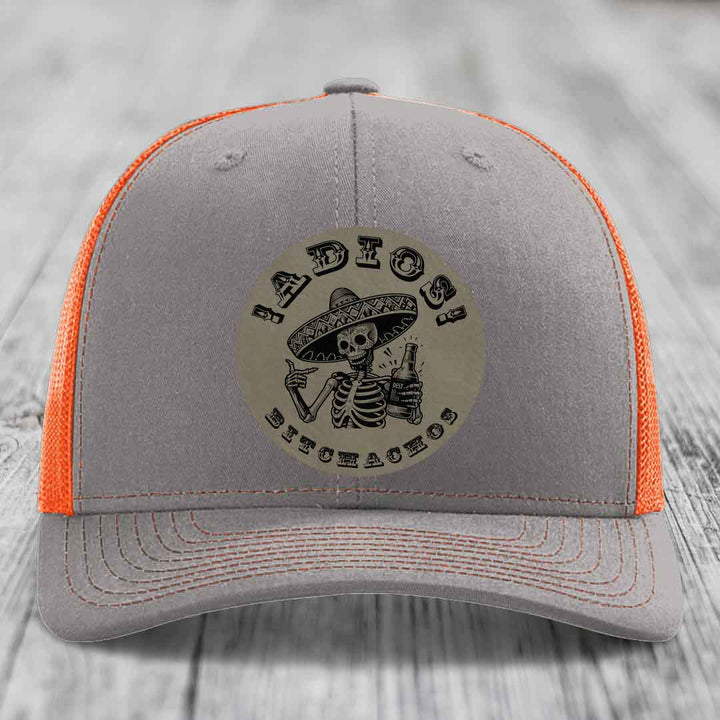 Grey trucker hat with orange mesh back and embroidered skull patch reading &