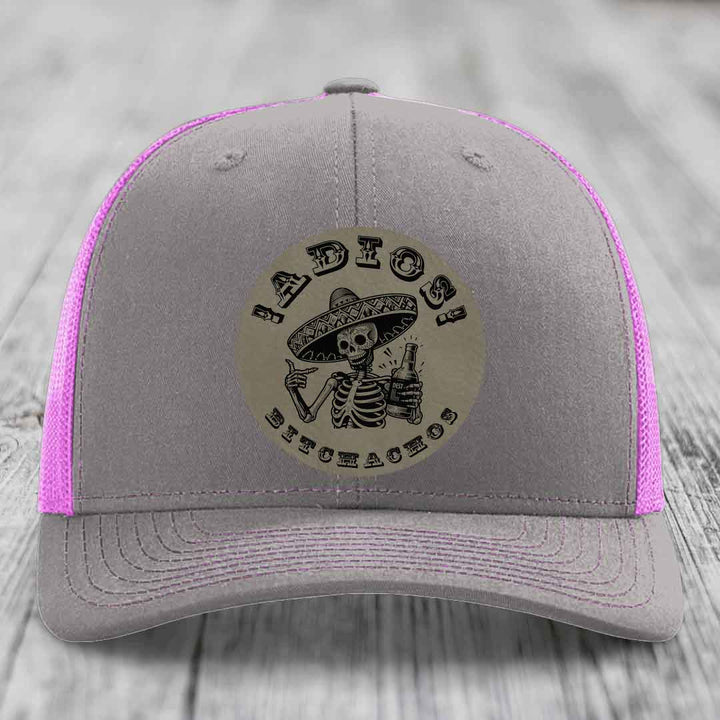 Grey trucker hat with pink mesh and stitching, featuring a circular patch of a skeleton in a sombrero holding a beer bottle with &