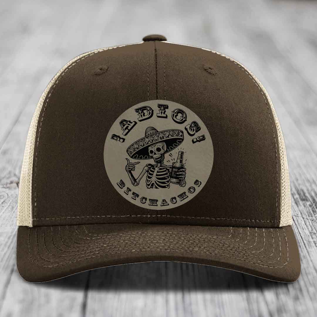 Brown trucker hat with beige mesh back and a circular patch featuring a skeleton in a sombrero holding a beer bottle.