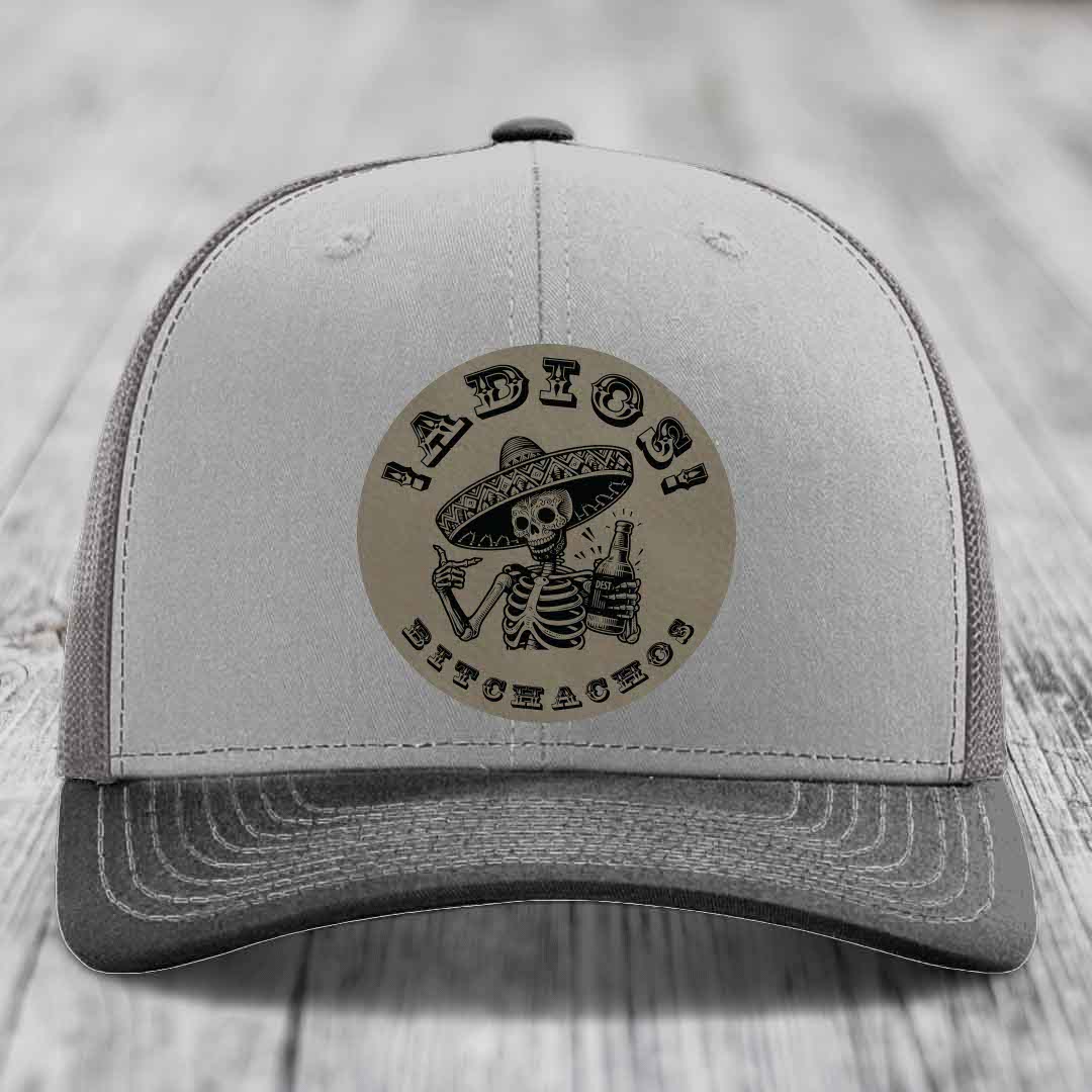 Grey trucker hat with circular leather patch featuring skeleton in sombrero holding beer bottle and text &