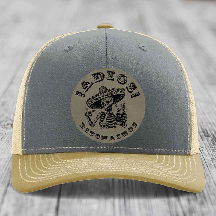 Grey and beige trucker hat with a circular leather patch featuring a skeleton in a sombrero holding a beer bottle.