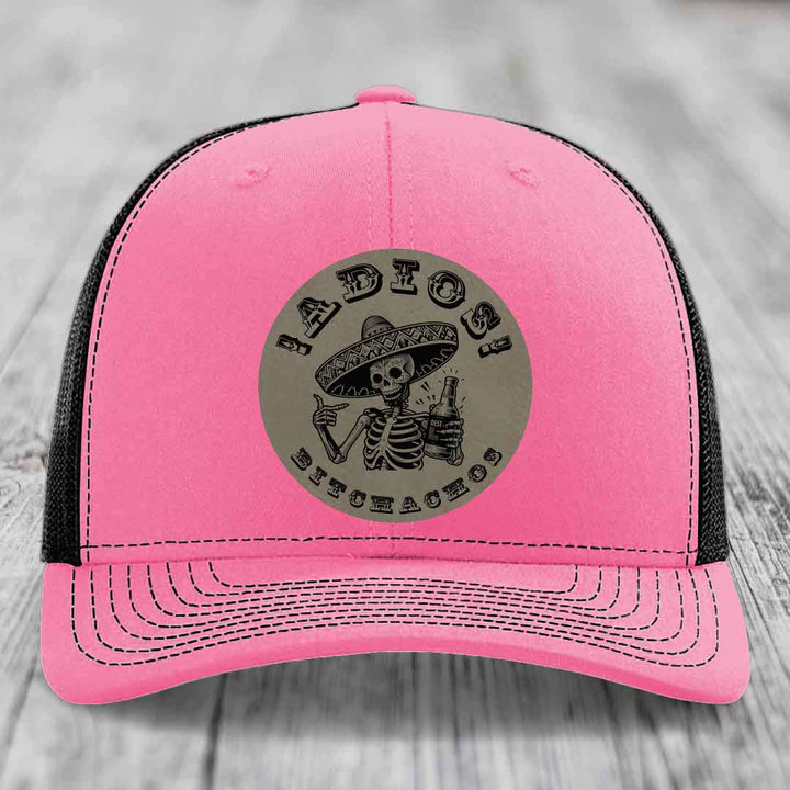 Pink trucker hat with black mesh back and gray circular patch featuring a skeleton in a sombrero holding a beer bottle with text &