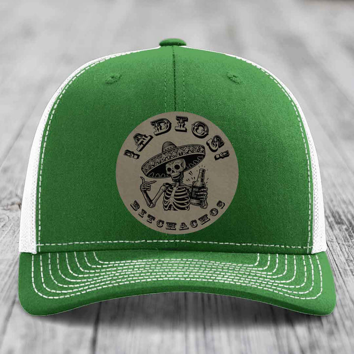 Green trucker hat with white mesh back and stitching, featuring a circular beige patch with a skeleton in a sombrero holding a beer bottle and the text &