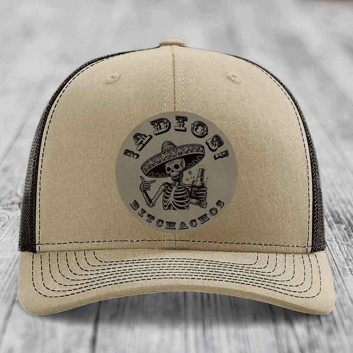 Beige trucker hat with black mesh back and embroidered skull graphic holding a beer bottle.
