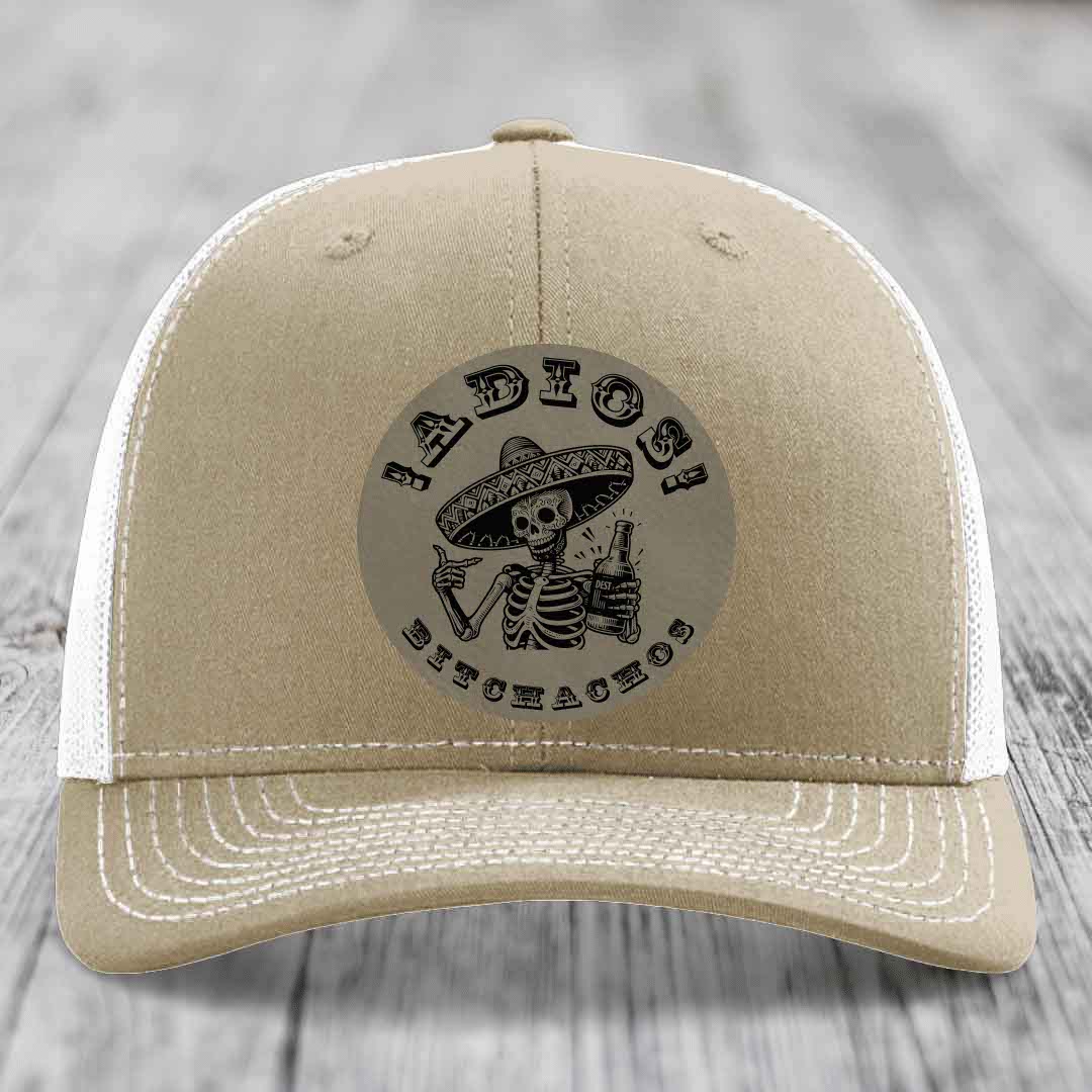 Tan trucker hat with black embroidered skull and sombrero patch reading &