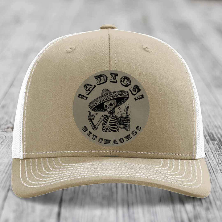 Tan trucker hat with black embroidered skull and sombrero patch reading &