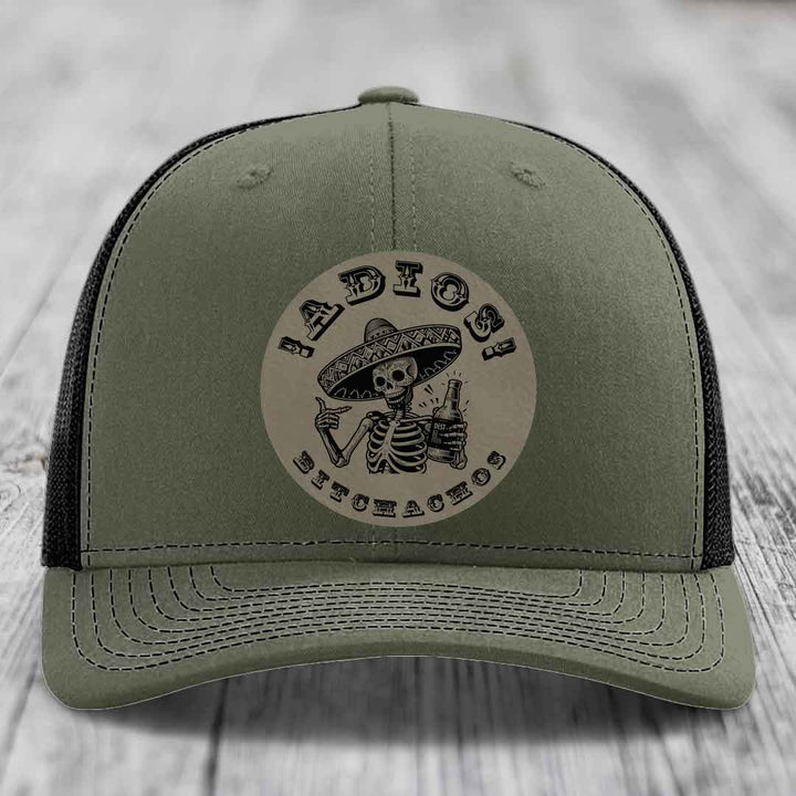 Olive green trucker hat with black mesh back and a circular patch featuring a skeleton in a sombrero holding a beer bottle.