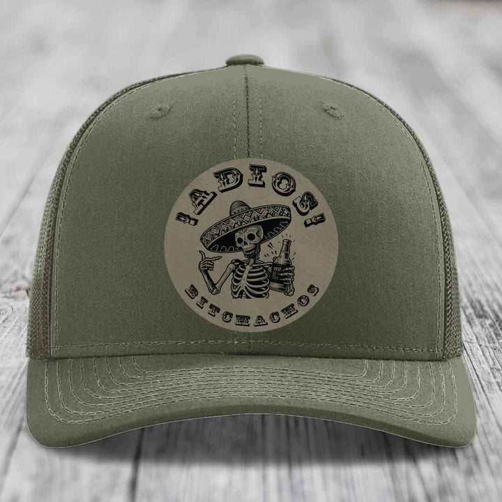 Olive green trucker hat with circular patch of skeleton in sombrero holding beer bottle and text &