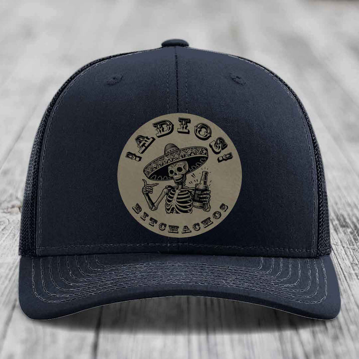 Dark blue trucker hat with a circular beige patch featuring a skeleton in a sombrero holding a beer bottle and the text &