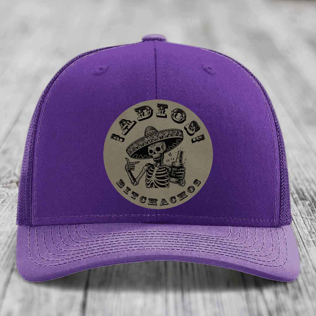 Purple trucker hat with circular beige patch featuring a skeleton in a sombrero holding a beer bottle and text &