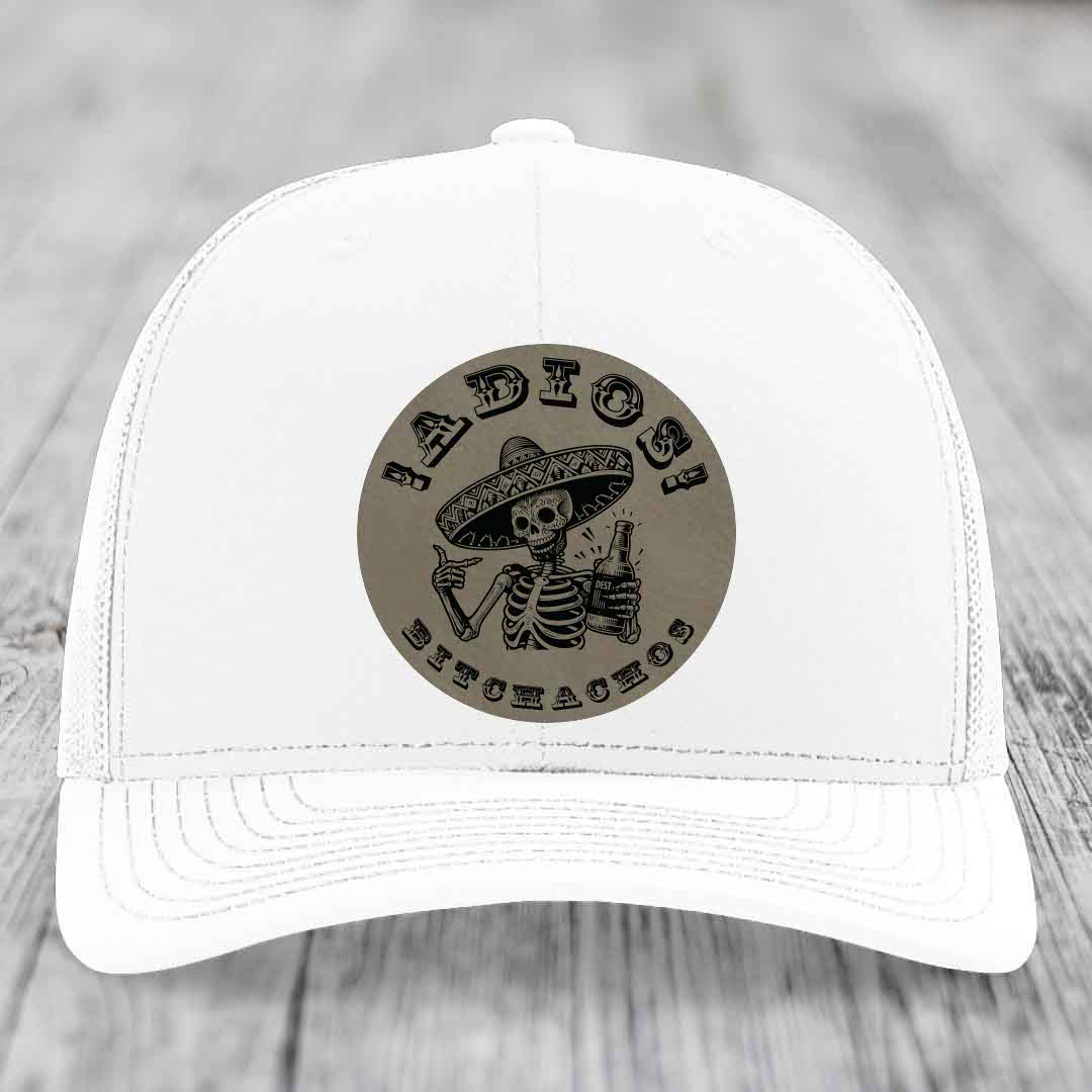 White trucker hat with a circular leather patch featuring a skeleton in a sombrero holding a beer bottle and the text &