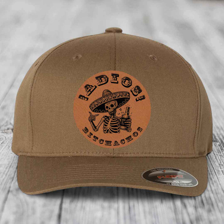 Tan baseball cap with circular brown leather patch featuring skeleton in sombrero holding beer bottle and text &