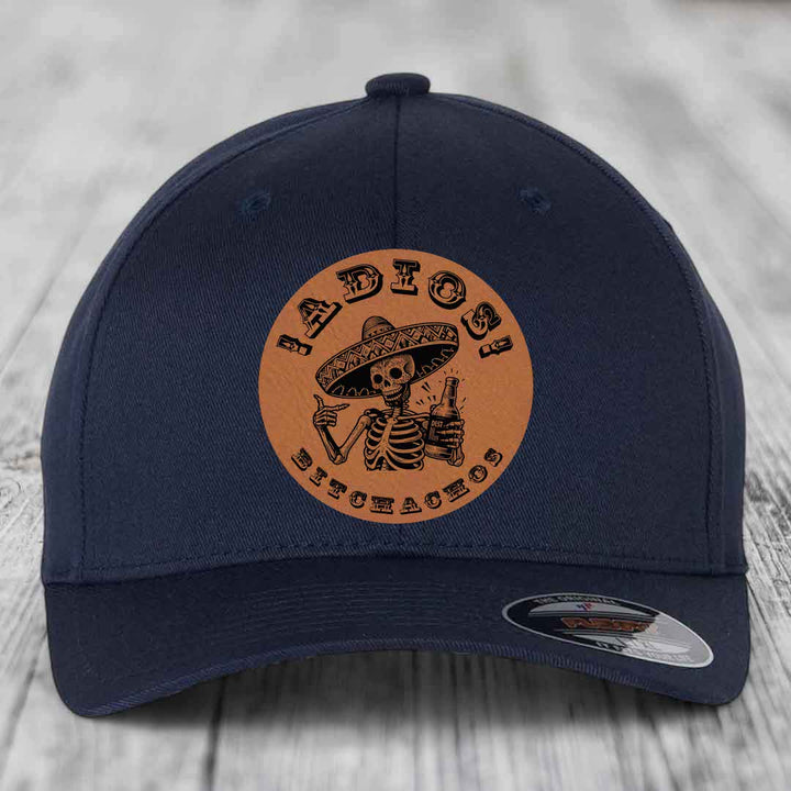 Dark blue baseball cap with circular tan leather patch featuring skeleton in sombrero holding beer bottle and text &