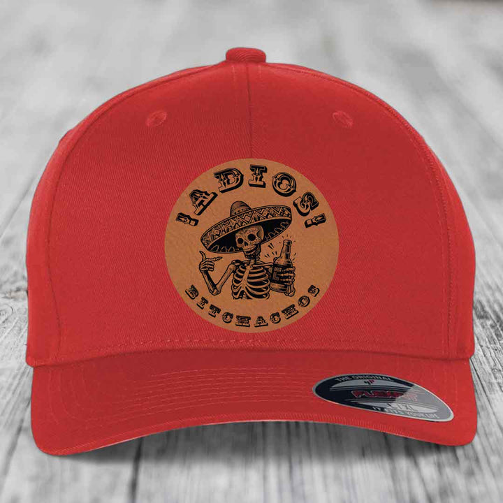 Red baseball cap with circular tan leather patch featuring skeleton in sombrero holding beer bottle and text &