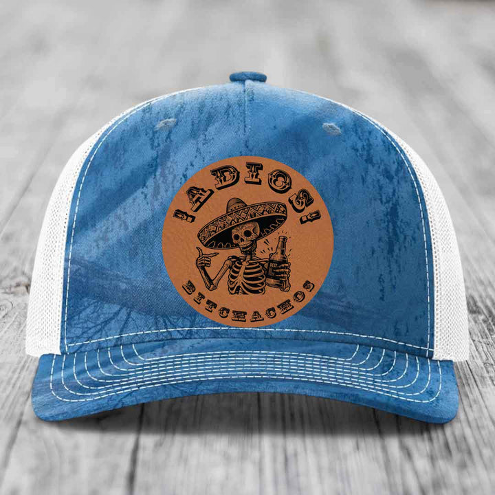 Blue and white trucker hat with a brown leather patch featuring a skeleton in a sombrero holding a beer bottle.