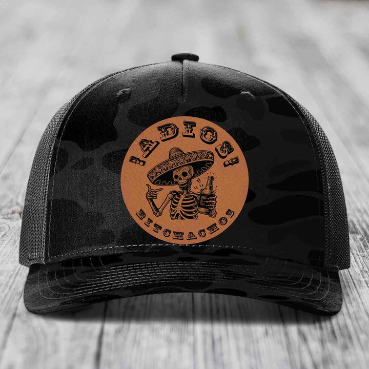 Black camouflage trucker hat with brown circular patch featuring skeleton in sombrero holding beer bottle.