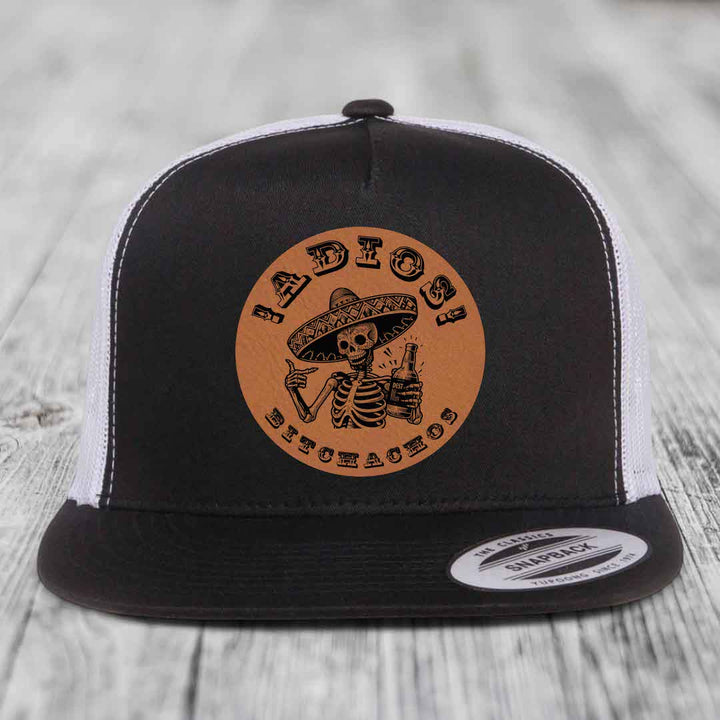 Black and white trucker hat with brown leather patch featuring skeleton in sombrero holding beer bottle.