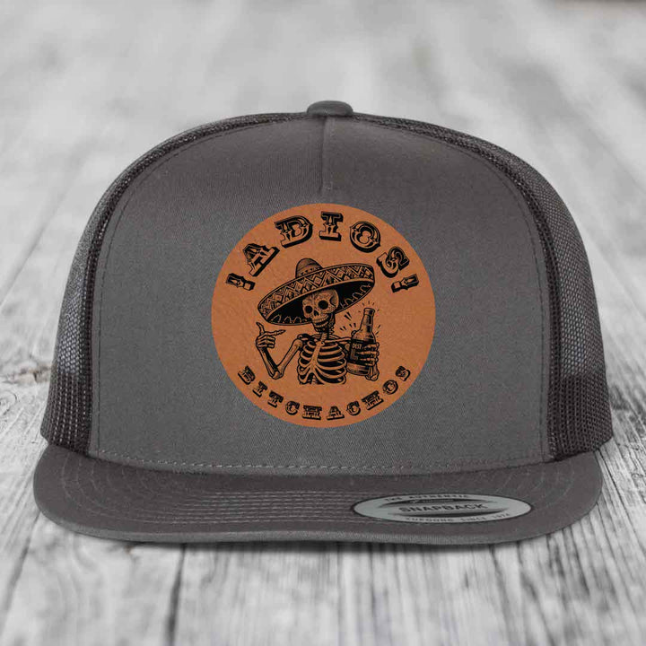 Grey trucker hat with brown leather patch featuring skeleton in sombrero holding beer bottle.