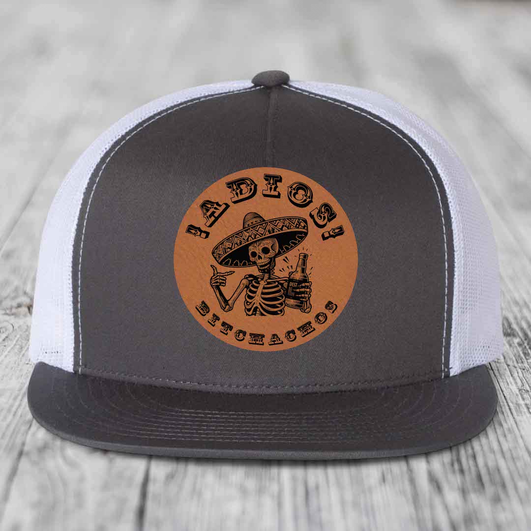 Grey and white trucker hat with brown leather patch featuring skeleton in sombrero holding beer bottle.