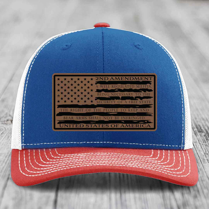 Blue and red trucker hat with a brown leather patch featuring the 2nd Amendment text and American flag design.