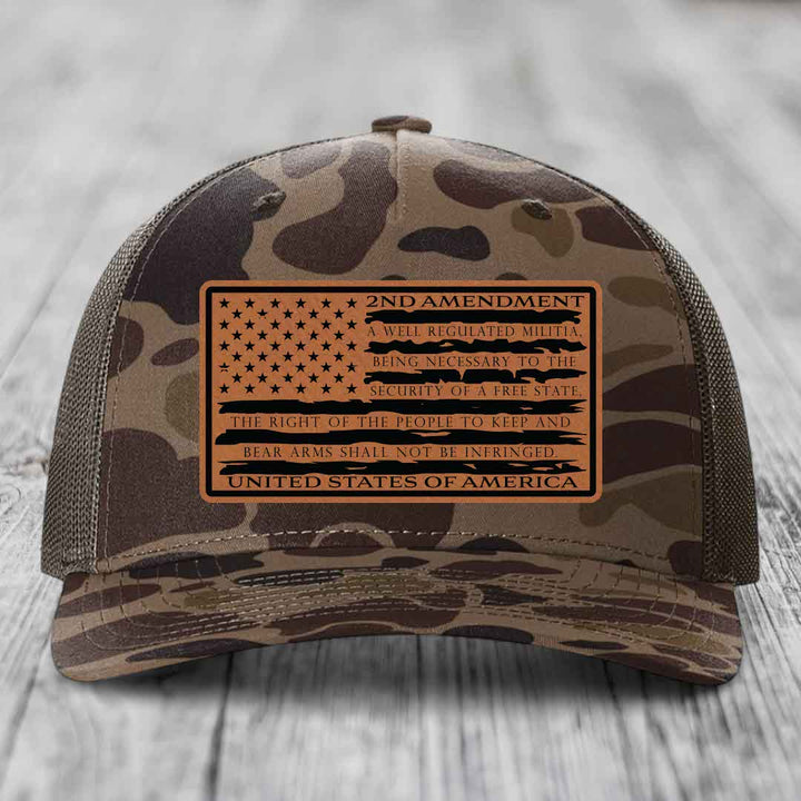 Camouflage trucker hat with a tan leather patch featuring the 2nd Amendment text and American flag design.