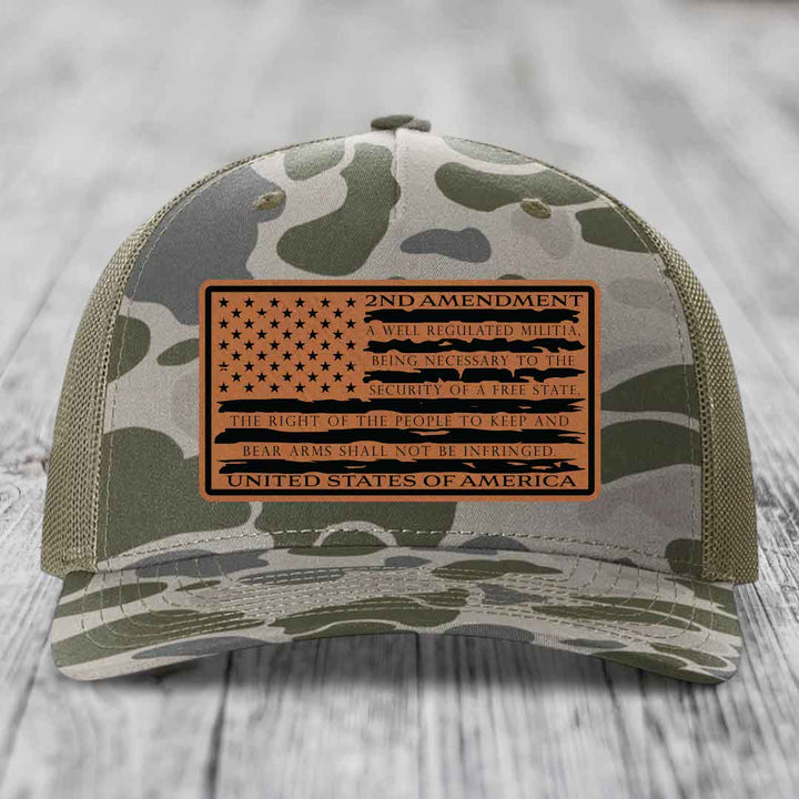Camouflage trucker hat with a tan leather patch displaying the 2nd Amendment text and American flag design.