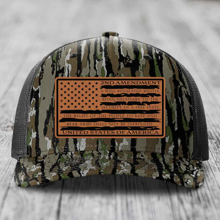 Camouflage trucker hat with a brown leather patch featuring the 2nd Amendment text and American flag design.