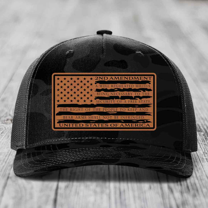 Black camouflage trucker hat with a tan leather patch featuring the 2nd Amendment text and American flag design.