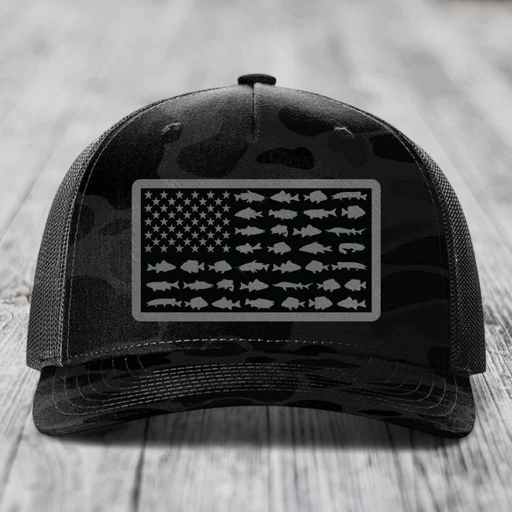 Black camouflage trucker hat with American flag patch made of fish silhouettes.