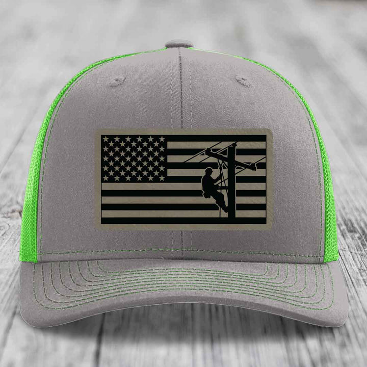 Grey trucker hat with neon green mesh and stitching, featuring an American flag patch with lineman silhouette.