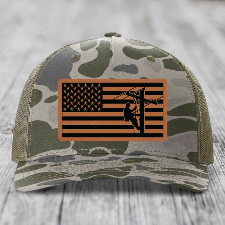 Camouflage trucker hat with American flag patch featuring lineman silhouette.