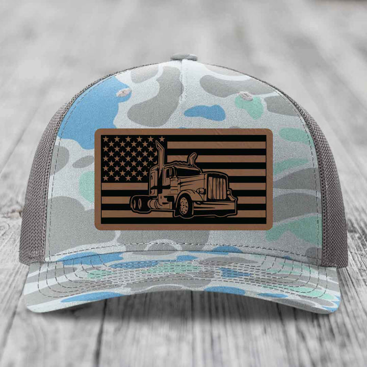 Camouflage trucker hat with American flag patch featuring Peterbilt truck design.