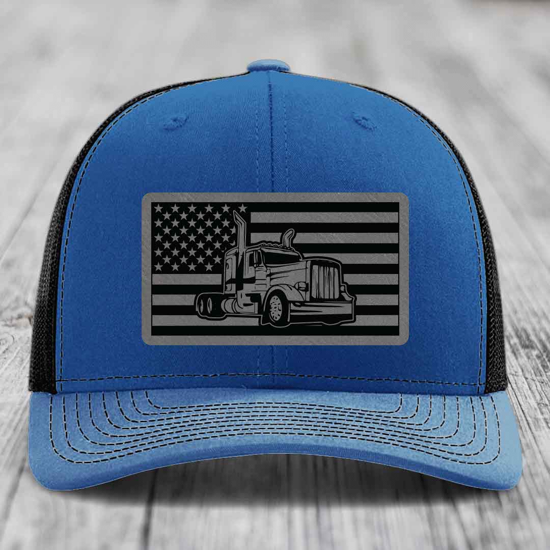 Blue trucker hat with black mesh back, featuring a rectangular patch of an American flag with a Peterbilt truck silhouette.