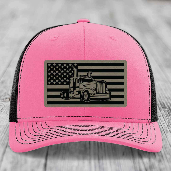 Pink trucker hat with black mesh back, featuring a rectangular patch of an American flag with a Peterbilt truck silhouette.