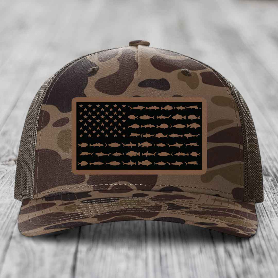 Camouflage trucker hat with American flag patch made of saltwater fish silhouettes in tan on black background.