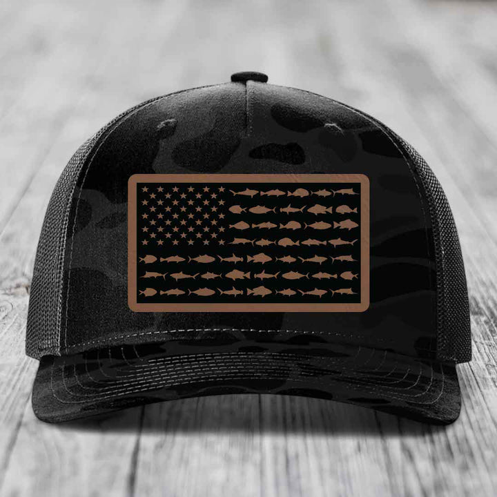 Black camouflage trucker hat with a rectangular patch featuring an American flag design made of fish silhouettes.