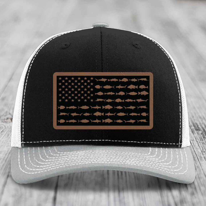 Black and white trucker hat with a brown leather patch featuring an American flag design made of fish silhouettes.