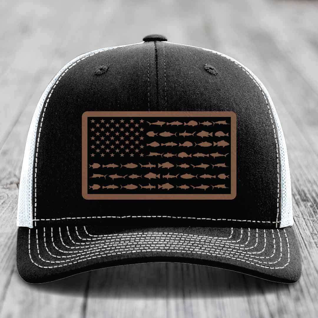 Black trucker hat with white stitching and a brown leather patch featuring an American flag design made of fish silhouettes.