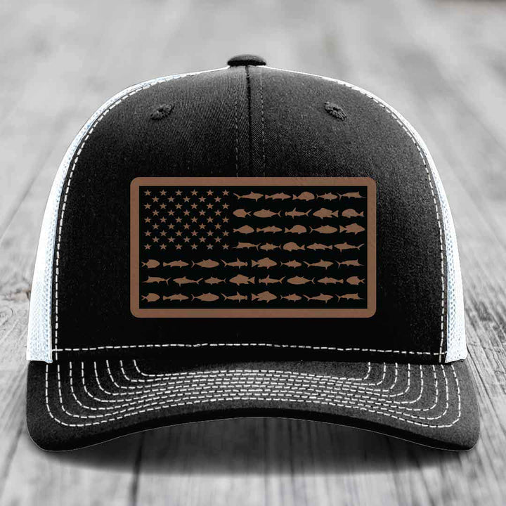 Black trucker hat with white stitching and a brown leather patch featuring an American flag design made of fish silhouettes.