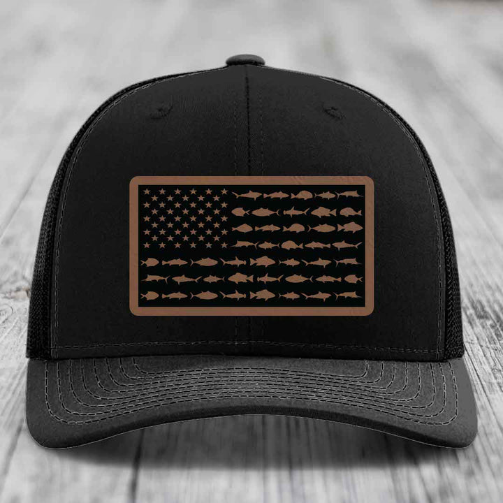 Black trucker hat with a brown leather patch featuring an American flag design made of fish silhouettes.