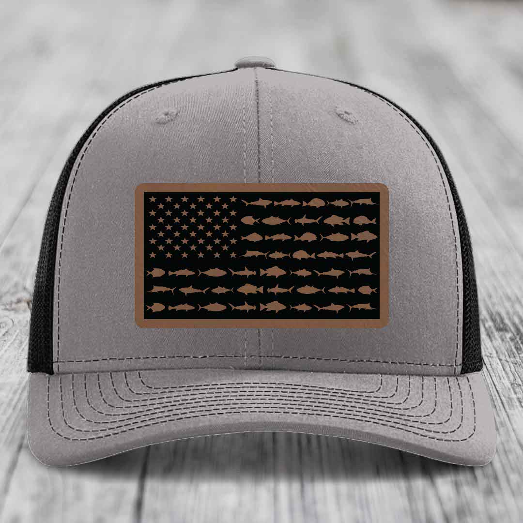 Grey trucker hat with black mesh back and a rectangular leather patch featuring an American flag design made of saltwater fish silhouettes.