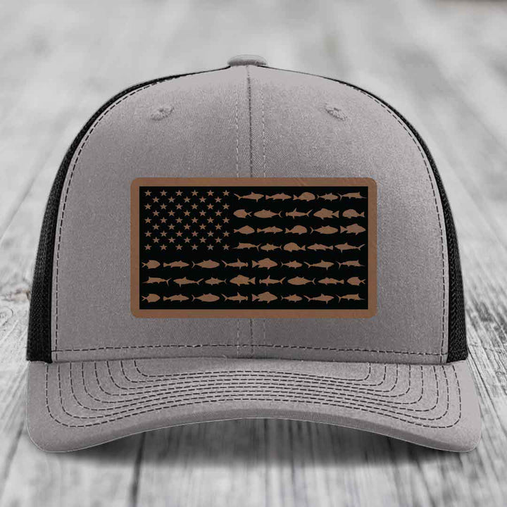 Grey trucker hat with black mesh back and a rectangular leather patch featuring an American flag design made of saltwater fish silhouettes.