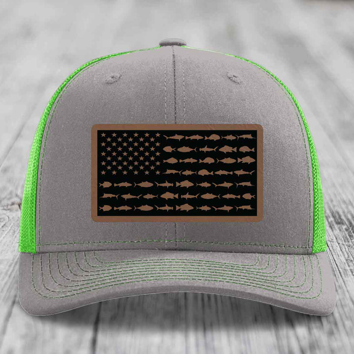 Grey trucker hat with neon green mesh and stitching, featuring a rectangular American flag patch made of brown leatherette with fish silhouettes replacing stars and stripes.