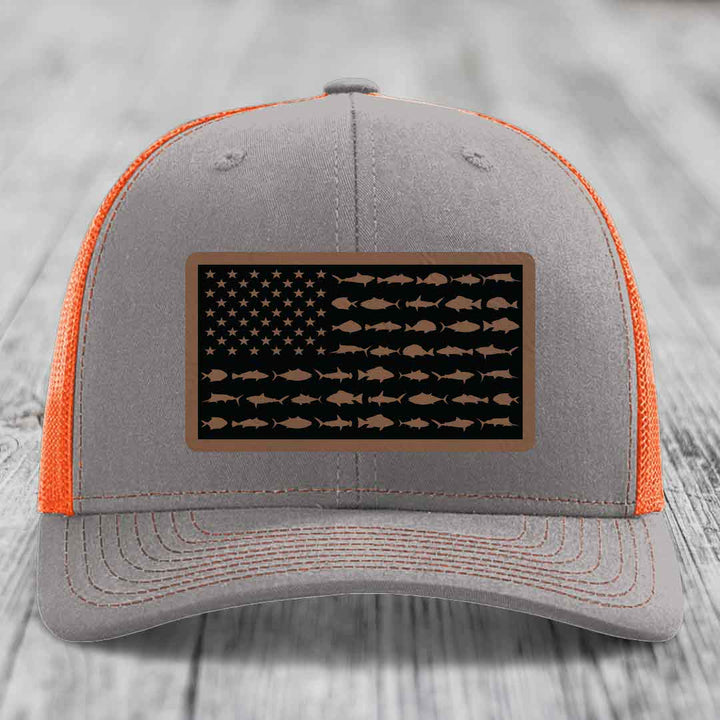 Grey trucker hat with orange mesh, featuring a saltwater fish American flag leather patch.